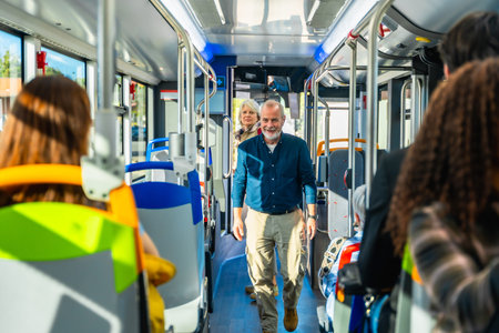 Senior man smiling and looking at the camera while walking down the aisle of a public bus, with other passengers seated and standing, representing urban transportation and daily commuteの写真素材