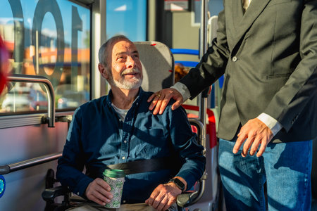 Young caregiver places hand on shoulder of smiling senior man in wheelchair during accessible public transport ride, sharing warmth, trust and comfortable mobilityの写真素材