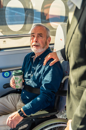 Senior man in a wheelchair receiving assistance from another person, highlighting support and accessibility during public transport travel and daily lifeの写真素材
