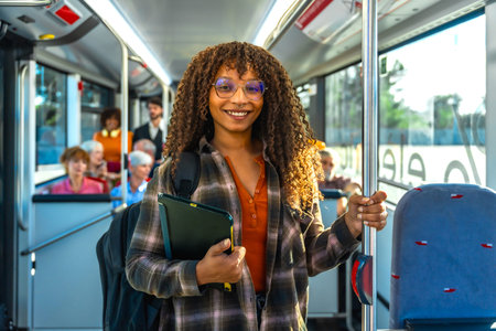 Young black woman student smiling at the camera while standing inside a public transportation bus,...