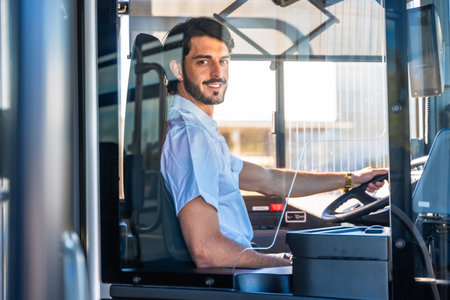 Young man working as a bus driver, smiling at the viewer while steering the public transport vehicle, representing professional occupation and serviceの写真素材