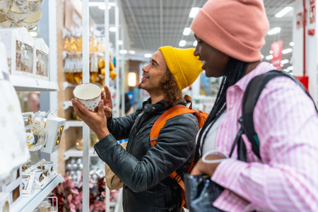 Young diverse couple browsing festive holiday decorations and gift ideas on department store shelves, smiling as they select seasonal presents and enjoy shopping togetherの写真素材