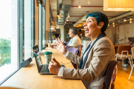 Business professional with headset actively communicating during an online video conference from a modern office workspace, discussing ideas and collaborating virtuallyの写真素材