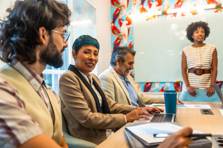 Diverse group of business colleagues meeting and collaborating in a modern office, sharing ideas and engaging in teamwork while one person delivers a presentationの写真素材