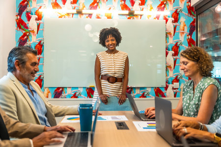 Diverse business team collaborating in a vibrant coworking space, discussing data charts and laptops while a confident presenter leads strategy, brainstorming and planning for successの写真素材