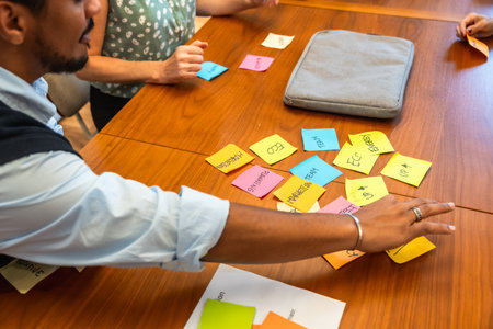 Business colleagues collaborating on a project, organizing ideas on a wooden table with colorful sticky notes during a corporate meeting, fostering teamwork and strategic planningの写真素材