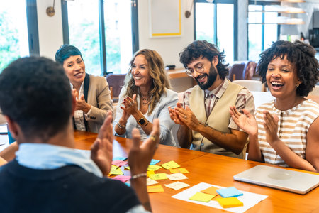 Diverse business colleagues celebrating successful ideas and achievements, clapping and smiling while participating in a collaborative meeting with sticky notes on the tableの写真素材
