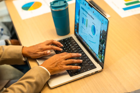 Person working on a laptop, hands typing on the keyboard, with a monthly performance review screen showing charts and graphs, indicating data analysis and business operationsの写真素材