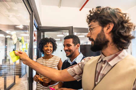 Diverse business colleagues collaborating and developing strategies, sticking colorful notes with ideas on a glass wall during an office brainstorming sessionの写真素材