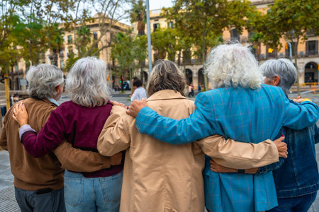 Group of diverse seniors walking together in a city, embracing with arms around each other, demonstrating strong friendship, support, and a sense of community outdoorsの写真素材