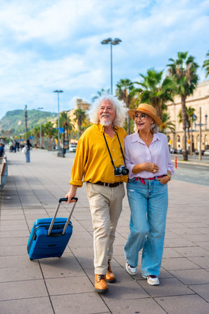 Smiling senior couple embracing a happy retirement, walking together with their luggage through a sunny city street, exploring and enjoying an exciting travel adventureの写真素材