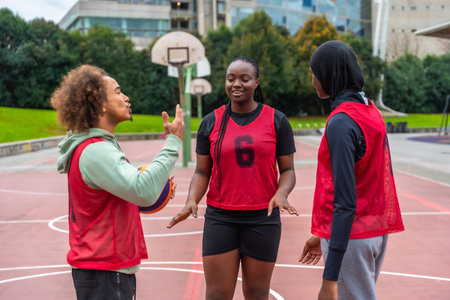 Diverse young adults on an urban basketball court talking strategy and bonding over streetball, collaborating as a confident, happy team during outdoor practice and playの写真素材