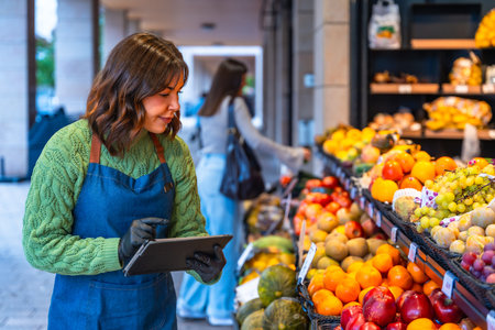 Woman in an apron and gloves managing inventory, checking stock levels of fresh fruit and produce on...