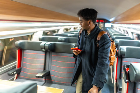 Young male passenger in a modern train carriage looking for his seat while checking travel information on a red smartphone during a business trip or commuteの写真素材