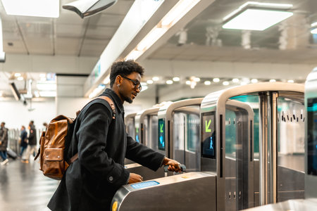 Young man with glasses and backpack tapping a contactless ticket at a modern subway turnstile,...