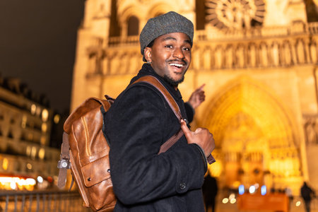 Young african american man smiling and pointing, enjoying a night out in Paris and exploring an...