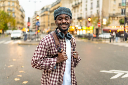 Young black man with headphones wearing a plaid shirt and backpack, standing confidently in a...