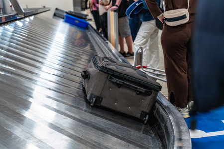 Passengers waiting at the baggage claim carousel in the airport, watching as a suitcase arrives on the conveyor belt. The atmosphere buzzes with anticipation and travel excitementの写真素材