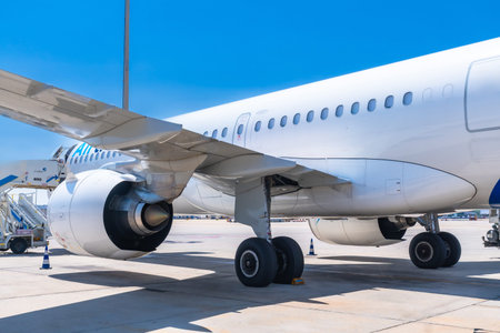 Passenger airplane parked on the runway airport, showing its wing, engine, and landing gear, under a...