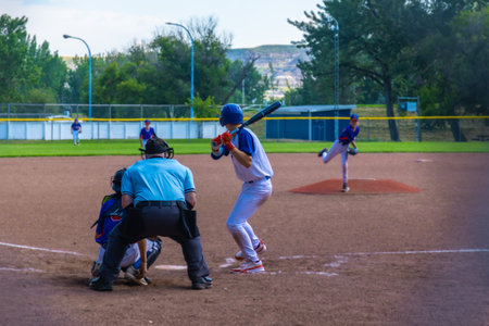 Teenage baseball batter waiting for the pitch while the pitcher is throwing the ball during a sunny...
