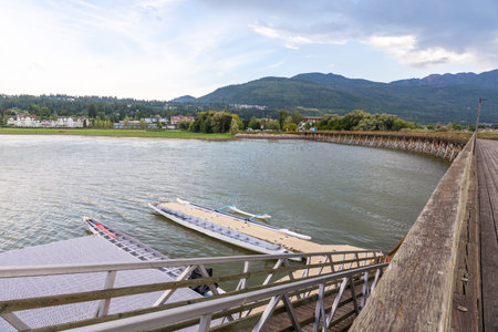 Boats are tied up at a floating dock near a wooden pier, with the city of salmon arm and the shuswap...