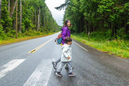 Mother and son crossing a paved road through lush rainforest in ucluelet, vancouver island, emphasizing road safety and family adventures in natureの写真素材