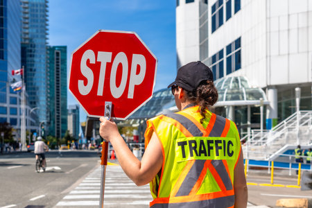 Traffic guard wearing high visibility vest holding stop sign regulating traffic flow on a city...