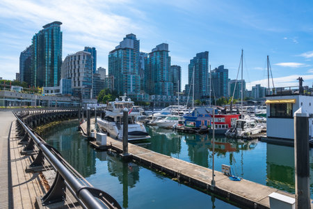 Modern buildings rise above a marina filled with yachts and houseboats, creating a picturesque scene reflecting in the calm waters, in Vancouver, British Columbiaの写真素材