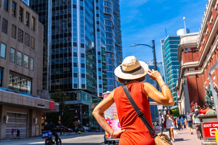 Female tourist wearing a straw hat and an orange dress is admiring the skyline of Vancouver, British Columbia, on a sunny summer day, enjoying the vibrant atmosphere and urban landscapeの写真素材