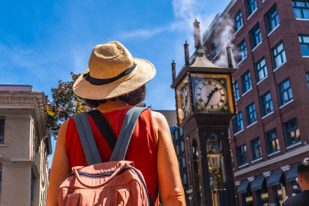 Female tourist wearing straw hat and backpack looking at the famous steam clock in Gastown historic district, Vancouver, British Columbia, Canada, on a sunny summer dayの写真素材