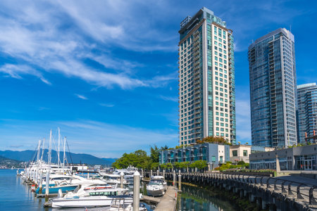 Modern residential skyscrapers rise majestically over the bustling harbor marina in Vancouver. British Columbia. On a sunny day with a vibrant blue sky and calm waters reflecting the cityscapeの写真素材