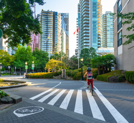 Canadian flag waving between modern buildings while a woman with backpack and helmet rides her bicycle in Vancouver downtown, British Columbiaの写真素材
