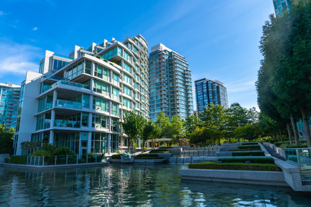 Modern glass and concrete buildings stand tall, reflecting in the calm water of a city park, creating a serene urban oasis in Vancouver, British Columbiaの写真素材