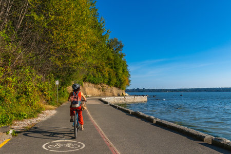 Tourist cycling through Stanley Park, soaking in stunning ocean views and vibrant cityscapes on a sunny summer day in Vancouver, British Columbia, Canadaの写真素材