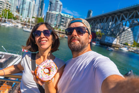 Happy tourists taking a selfie while holding a donut with sprinkles in front of the cityscape and...