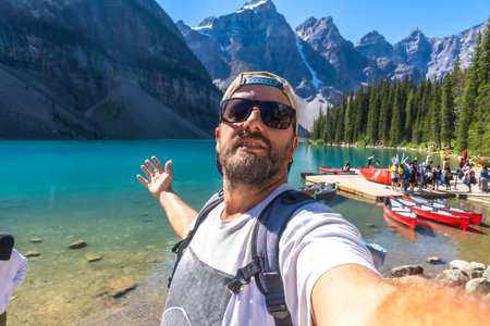 Backpacker taking a selfie with turquoise lake and canoes with the canadian rockies in the background at moraine lake in banff national park, alberta, canadaの写真素材
