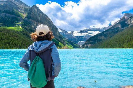 Female tourist admiring stunning turquoise waters of lake louise, framed by victoria glacier and the majestic canadian rockies in banff national park on a sunny summer dayの写真素材