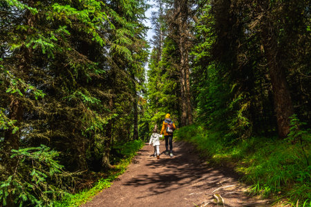 Mother and child walking on a path in a lush green forest near Maligne Lake in Jasper National Park,...