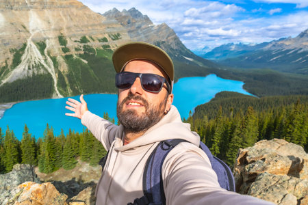 Hiker taking a selfie with outstretched arms, embracing breathtaking turquoise waters of Peyto Lake, surrounded by majestic mountains and lush forests in Banff National Parkの写真素材