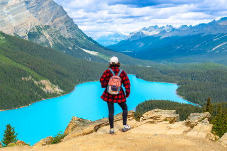 Female hiker standing on a cliff, soaking in the stunning panoramic view of turquoise Peyto Lake and the Canadian Rockies in Banff National Park, Alberta, on a sunny dayの写真素材