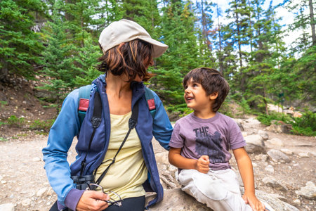 Mother and son taking a break during a hike in Mistaya Canyon, Banff National Park, enjoying a joyful moment amidst lush pine trees and rocky pathsの写真素材