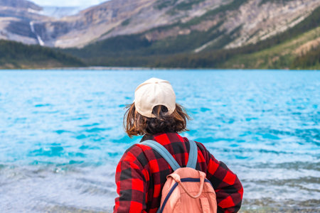 Young hiker with backpack and cap enjoying the breathtaking view of bow lake and surrounding mountains in Banff National Park, a stunning natural wonder in the Canadian Rockiesの写真素材