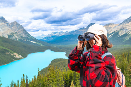 Female hiker using binoculars, admiring the scenic turquoise waters of Peyto Lake and the majestic mountains in Banff National Park, Alberta, Canadaの写真素材