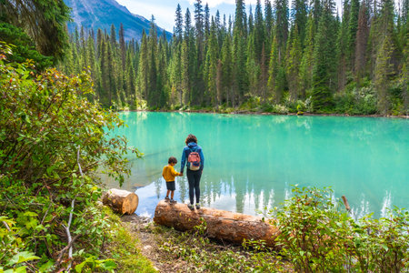 Mother and son holding hands on a log, enjoying the stunning turquoise waters of emerald lake, surrounded by lush forests and mountain peaks in Banff National Parkの写真素材
