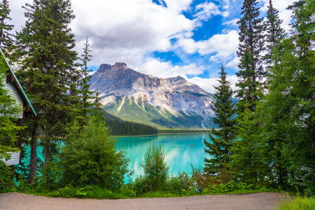 Emerald lake reflecting the majestic mount burgess under a cloudy sky, surrounded by lush vegetation and a wooden cabin in Banff National Park, Albertaの写真素材