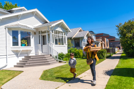 Mother and son carrying packages walking on a sidewalk in a residential neighborhood in Calgary, Alberta, enjoying the sunny summer weather and the beautiful housesの写真素材