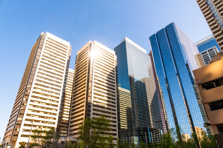 Sunlight illuminates the impressive skyscrapers of Calgary's downtown core, showcasing the city's modern architecture and bustling urban landscape against a clear blue skyの写真素材