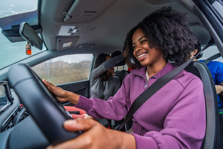 Smiling black woman driving with diverse friends, enjoying a carefree road trip, candid in car...