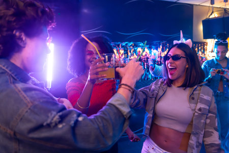 Group of young diverse friends enjoying an exciting night out, cheering with cocktails and dancing...