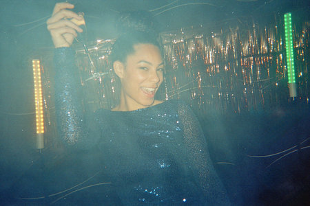 Woman in a sequined dress raising a champagne glass with an excited smile, celebrating with friends...